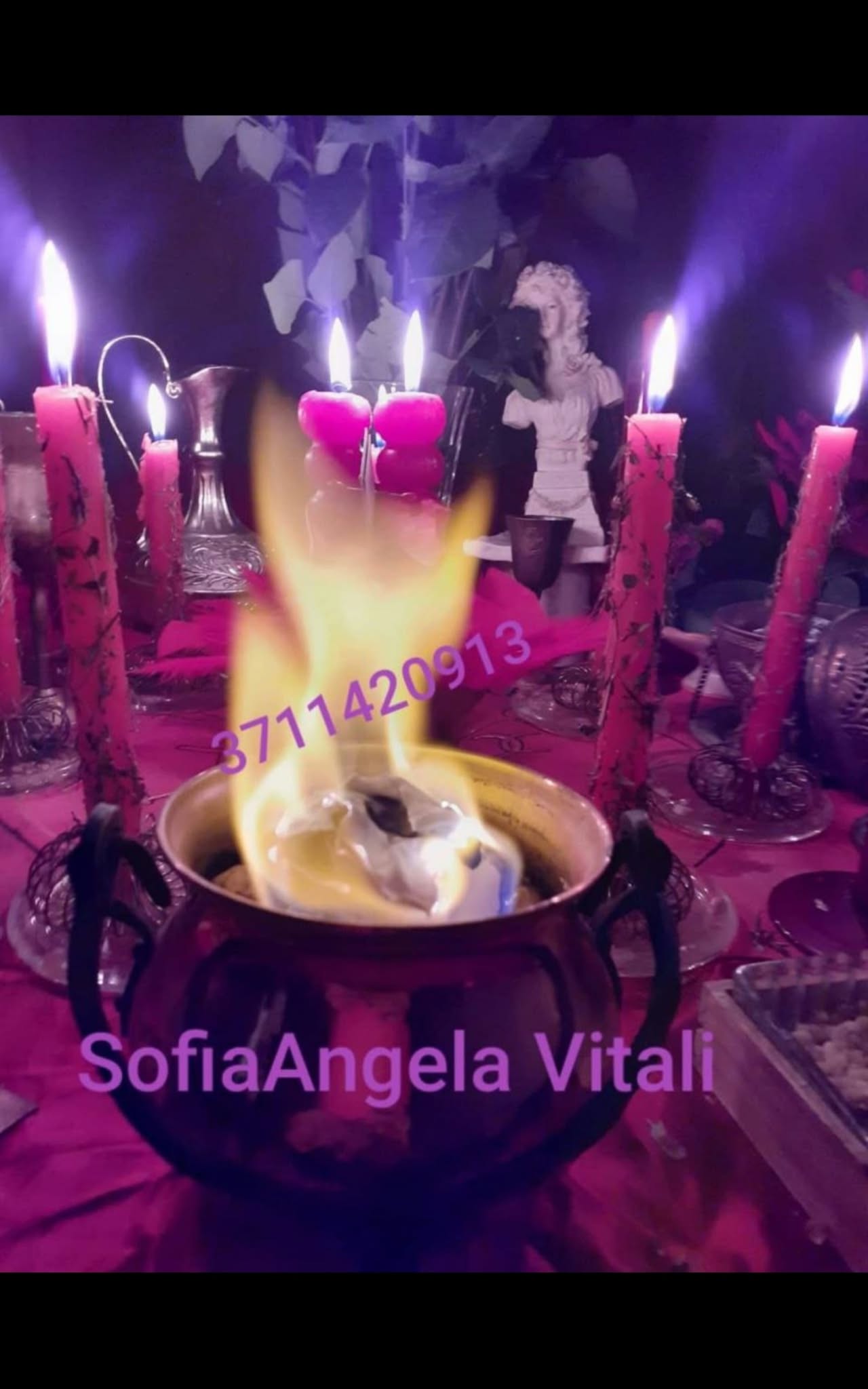 A close-up of a metal bowl with a bright flame, surrounded by pink candles and a small statue in purple lighting.