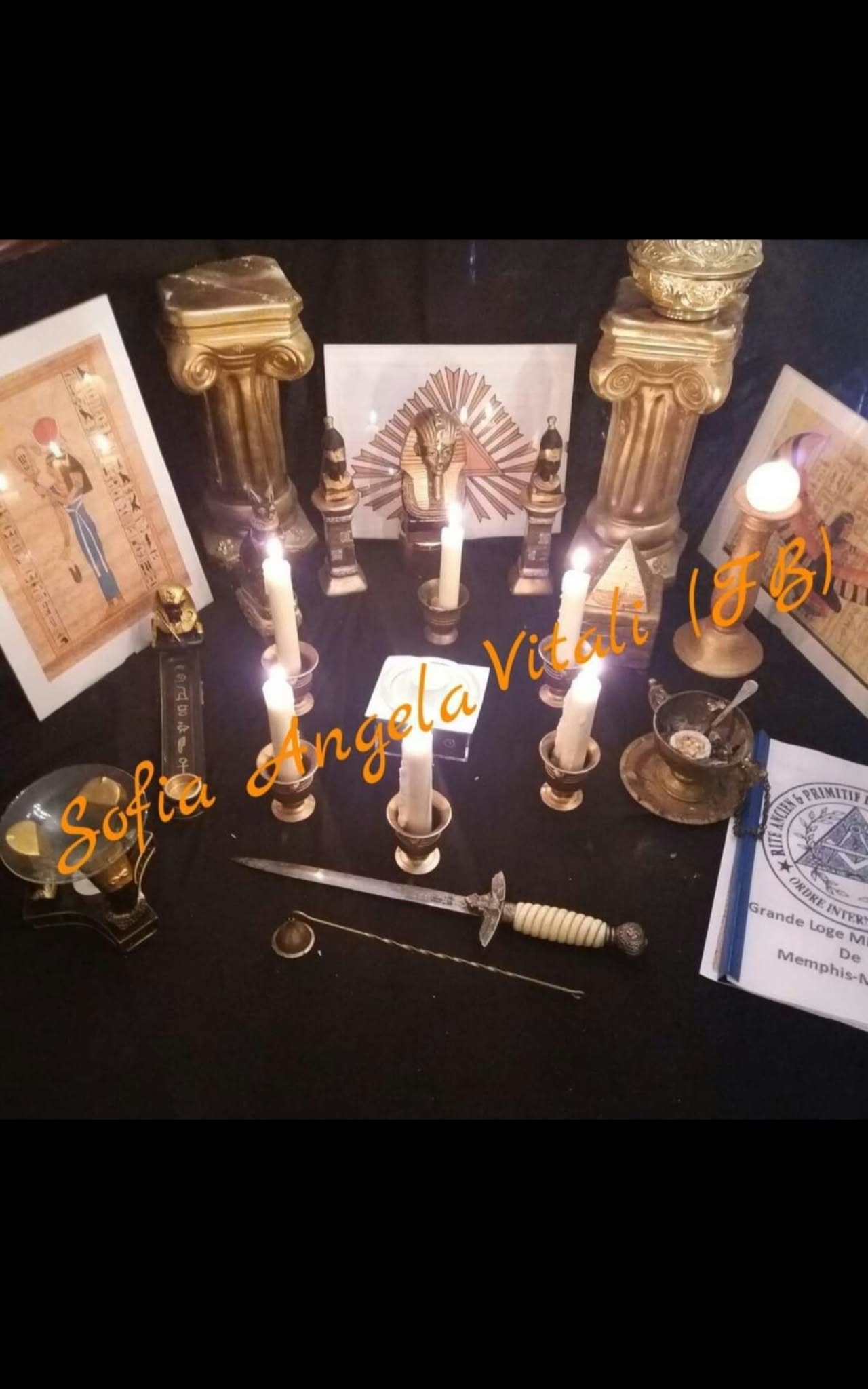 A symmetrical tabletop display with candles, columns, framed artwork and small objects, photographed from above under low warm lighting.