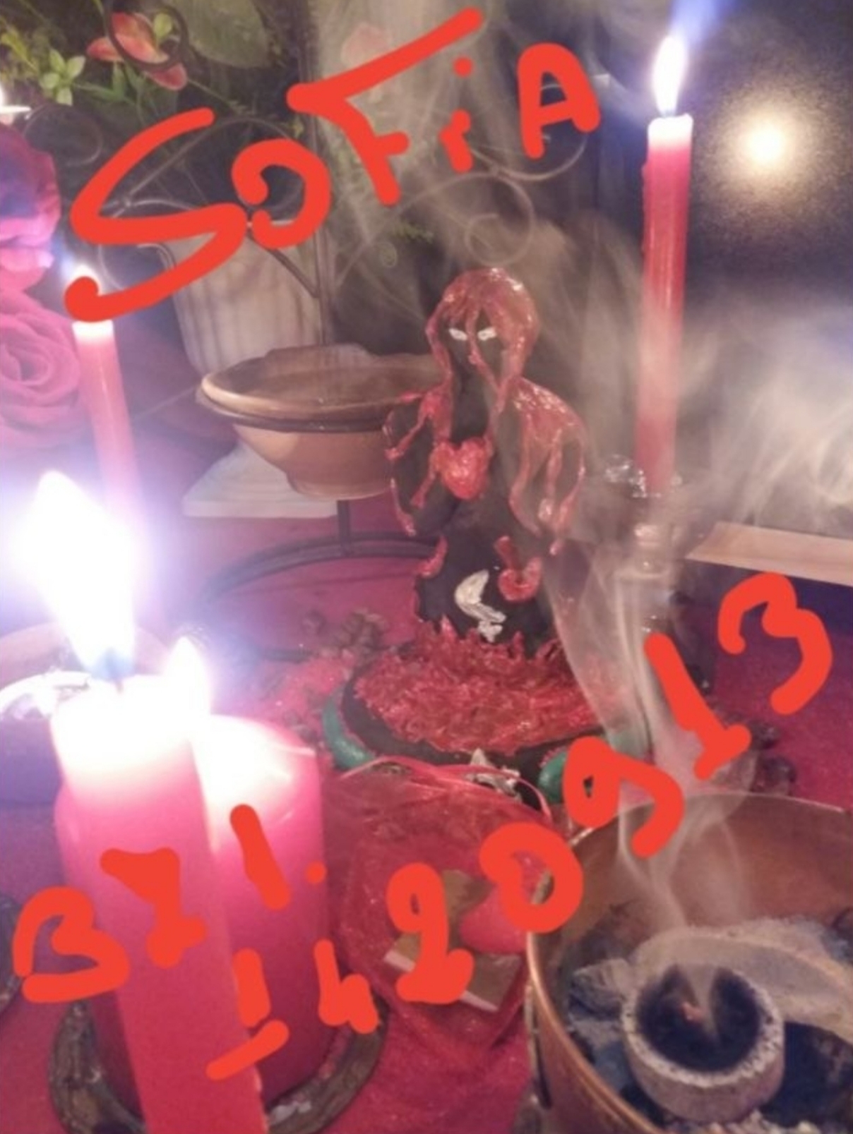 A candlelit arrangement with a small central figurine, red candles, smoke and large red handwritten text.