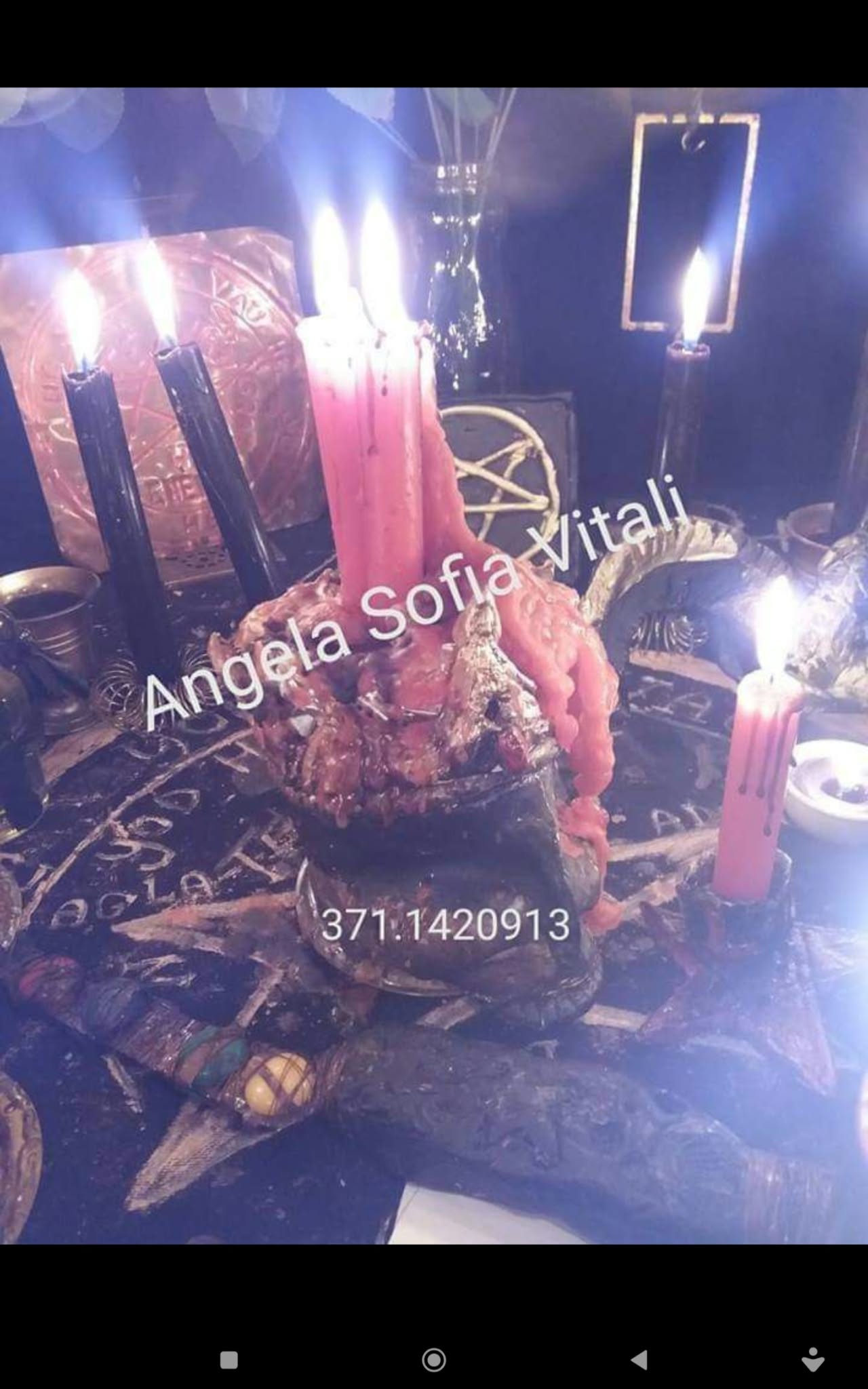 A close-up of a central candle arrangement with red and black candles, a pale sculptural object and bright glare from the flames.